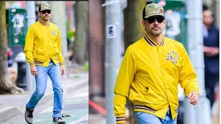 Bradley Cooper wears a bright yellow bomber jacket that says Muhammad Ali 1974 on the front and Peop