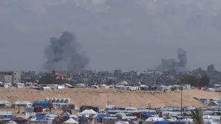 Plumes of smoke rising behind buildings seen from Muwasi in direction of East Rafah