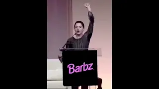 Rose McGowan standing on a Barbz podium shouting, "We are here!"