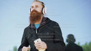 Happy young bearded hipster man with headphones and smartphone listen to music and dancing on city