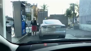 Женщина заправляет электромобиль Теслу бензином.