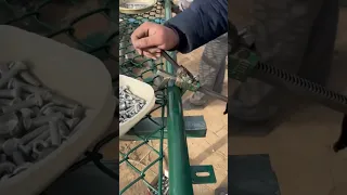 Worker installing steel mesh fence gate simply with his special tool
