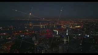Aerial descending footage of city centre and large seaport at night. Illuminated buildings and