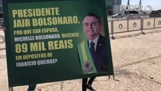 Manifestantes seguram cartazes questionando depósitos feito por Queiroz para Michelle Bolsonaro