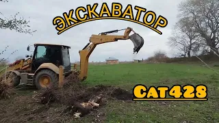 (ЭКСКАВАТОР CAT 428).CAT 428 excavator breaks tree roots with a small bucket