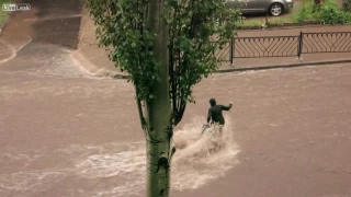 Woman tries to cross a flood but gets dragged down the road anyway.