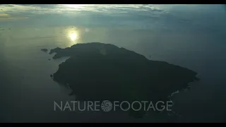 Very high aerial of Cocos Island at dawn, with sun's reflection on the ocean in the background