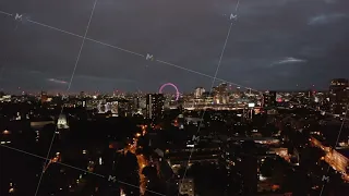 Descending shot of night cityscape. Urban neighbourhood at night. Illuminated London Eye in distance