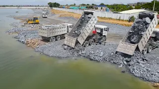 Team Operator Bulldozer Push Stone Into Deep Water with Dump Truck Unloading Stone Filling Huge Lake