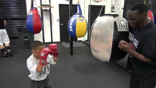 Jeff Mayweather instucting a little kid on the uppercut bag inside the Mayweather Boxing Club