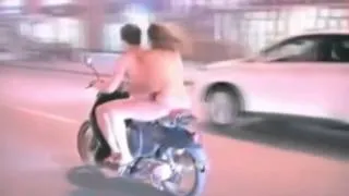 Голые девушка и парень едут на мотоцикле по улице.