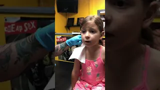 Little girl get her ears pierced for the first time at a tattoo parlor.