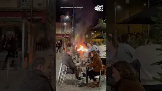 Diners enjoy wine amid the glow of a fire lit by demonstrators in France