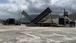 Trucks are stockpiling gravel on the ground because the ship has not docked yet due to rough seas.