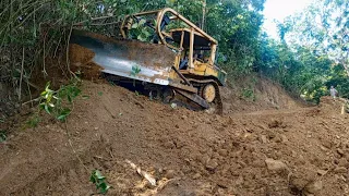 High-risk work D6r Xl bulldozer works to cut hills to lower plantation road inclines