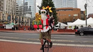 Santa plays flaming bagpipes with one hand while holding a pile of presents in downtown Portland