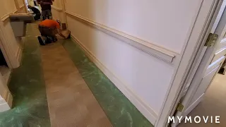 Commercial wall trimmer cutting down carpet tile on wood baseboard that is on the floor