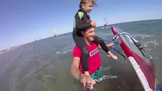 Guy Windsurfs With Little Girl on Shoulders