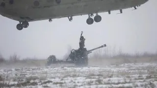 Soldiers difficulty attach an M119A3 Howitzer to a CH-47 Chinook Helicopter middle of a snowstorm