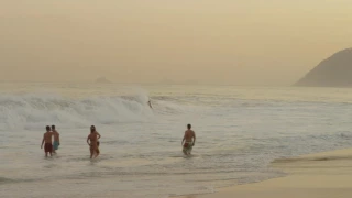 Slow motion pan of surfers and people enjoying Ipanema beach