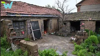 A middle-aged women renovate an old stone house next to a beautiful river