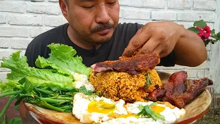 eating crispy pork with fried rice, half fried egg, lettuce and spicy dry bamboo shoots soup.