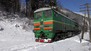 A powerful diesel locomotive pulls a passenger train up at the foot of a snow-covered mountain