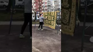 Женщина выбивает ковёр на детской площадке