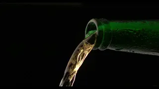 BEER IS POURED OUT OF A GREEN GLASS BOTTLE BLACK BACKGROUND 4K