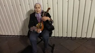 An old woman with bandaged fingers plays the Russian balalaika