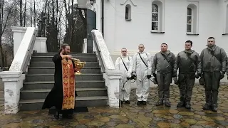 Батюшка окропляет солдат, дезинфицирующих церковь