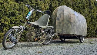 A bicycle camper pulled by a motorized custom tow bike.