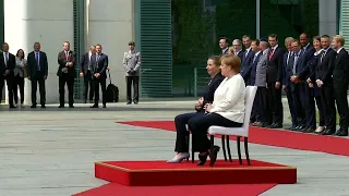 Angela Merkel sits for military honours after being seen shaking three times