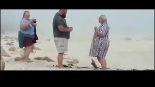 WATCH : women falls three times while trying to capture beach proposal