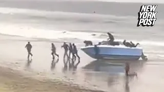 VIDEO: Dozens of migrants rush past shocked CA beachgoers after speedboat suddenly washes ashore