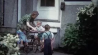 1944: Mother readies tricycle bike for kids playing outside family home.  PORTLAND, OREGON